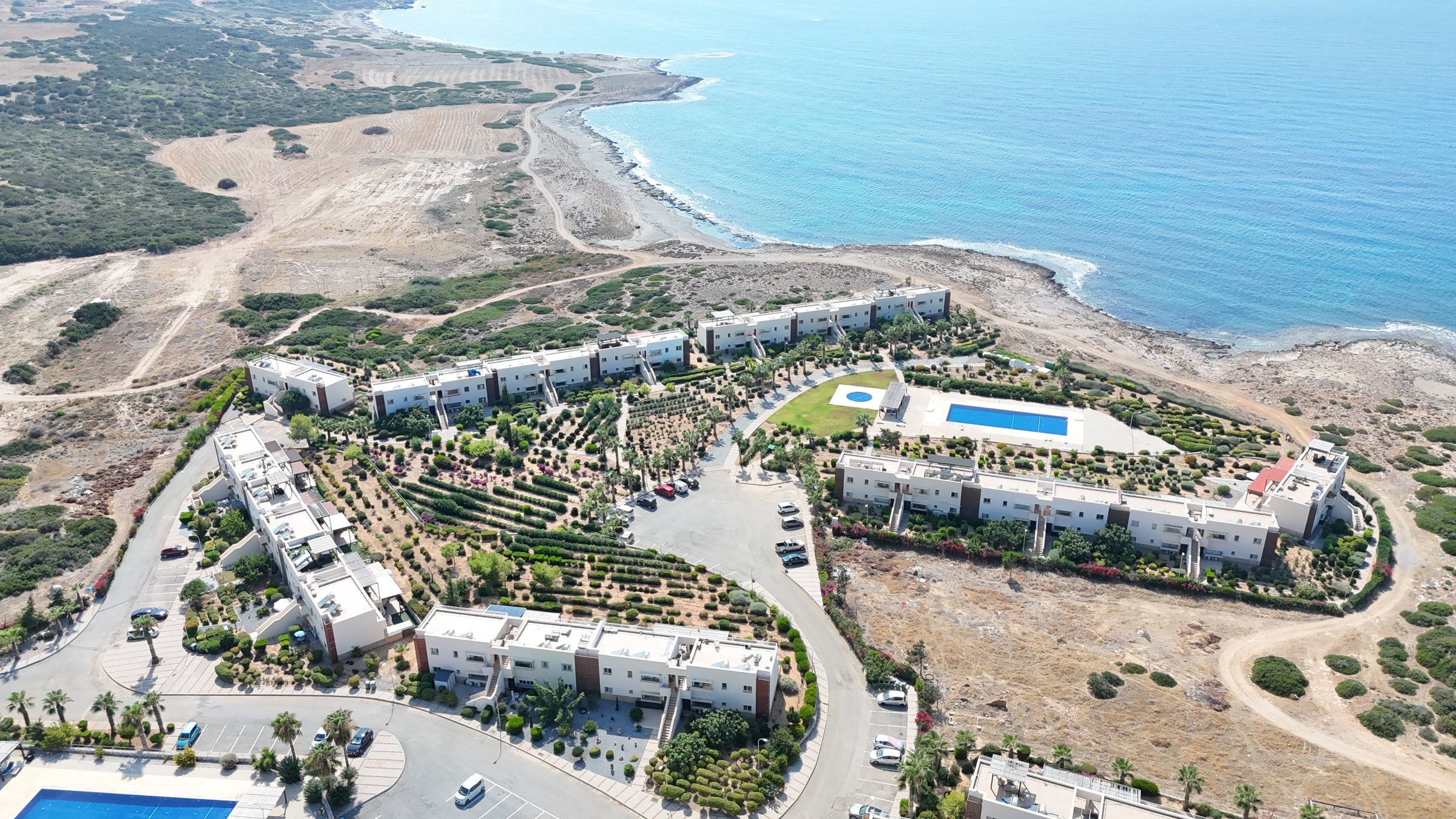 An apartment site with terraced gardens and shared pools above a turquoise bay